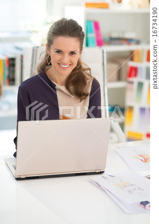 Smiling fashion designer working on laptop in office 16734190
