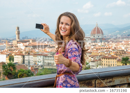 Happy young woman taking photo of panoramic view of florence, it 16735198