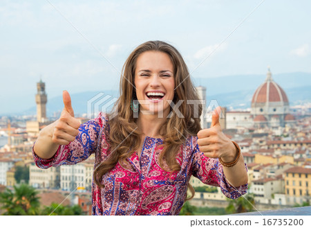 Smiling young woman showing thumbs up against panoramic view of 16735200
