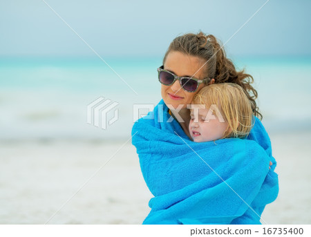 Mother and baby girl wrapped in towel sitting on beach Mother and baby girl wrapped in towel sitting on beach 16735400