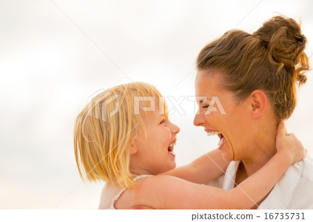 Stock Photo: Portrait of laughing mother and baby girl hugging on beach at th