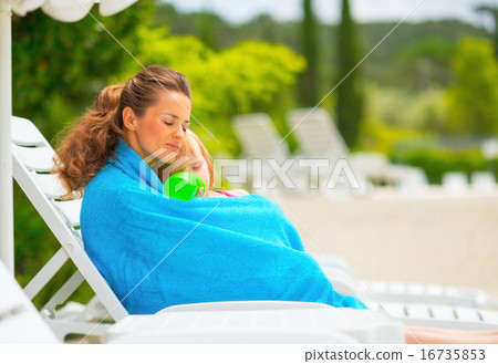 Mother and baby girl wrapped in towel sitting on sunbed 16735853