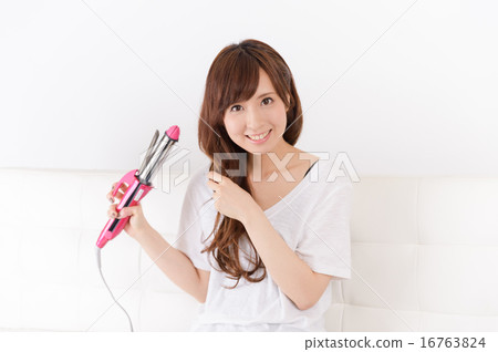 A young woman using a hair iron A young woman using a hair iron 16763824