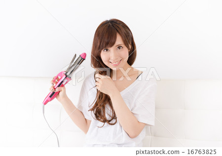 A young woman using a hair iron A young woman using a hair iron 16763825