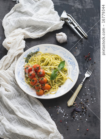Pasta spaghetti with pesto sauce, basil, baked cherry-tomatoes on rustic wooden tabke dark table 16779344