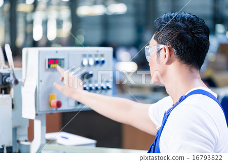 Worker pressing buttons on CNC machine 16793822