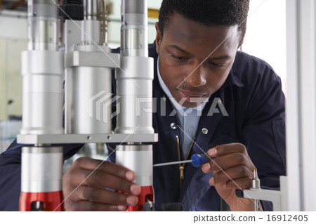 Male Apprentice Engineer Working On Machine In Factory Male Apprentice Engineer Working On Machine In Factory 16912405