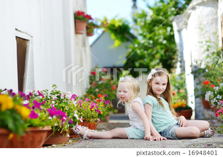 Two adorable little sisters sitting among flowers Two adorable little sisters sitting among flowers 16948401