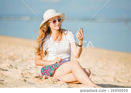 Beautiful young woman on the beach at sunny day with mobile phone 16950850