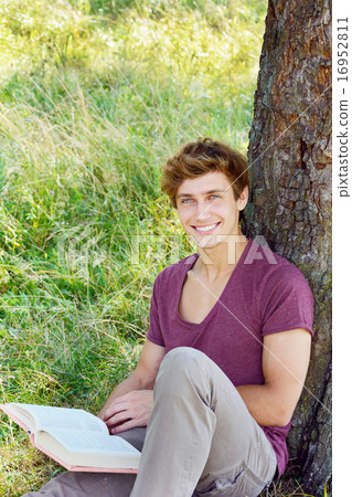 Young man is sitting and reading a book Young man is sitting and reading a book 16952811