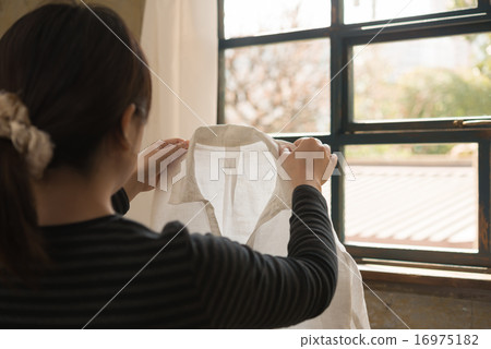 A woman's daily routine: checking the finish of her shirts by the window. A woman's daily routine: checking the finish of her shirts by the window. 16975182