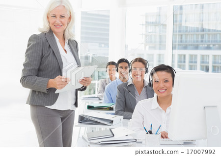 Smiling businesswoman looking at camera while work team using co Smiling businesswoman looking at camera while work team using co 17007992