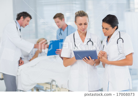Doctors looking at clipboard while theirs colleagues speaks with 17008073