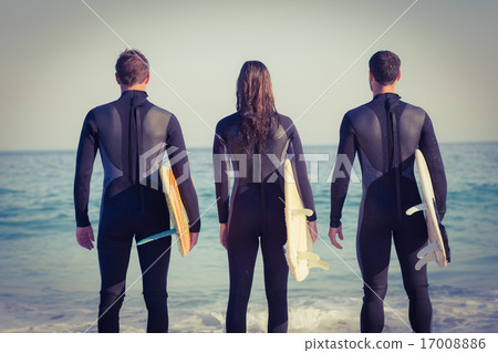 Friends on wetsuits with a surfboard on a sunny day 17008886