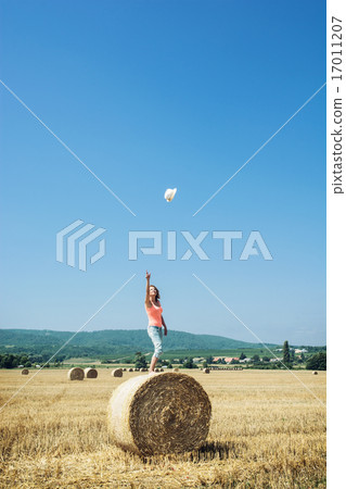 Young woman stands on the haystack and throws her hat high into 17011207