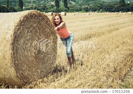 Smiling woman pushing the haystack and having fun by harvest Smiling woman pushing the haystack and having fun by harvest 17011208