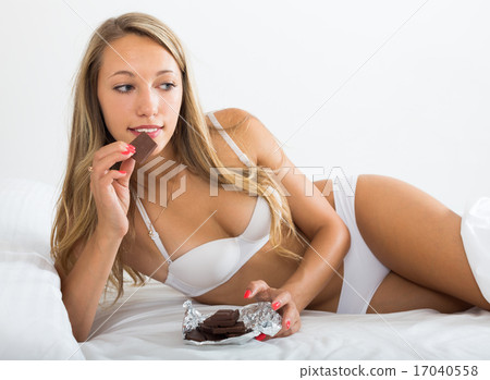 Woman in white eating chocolate in her bed 17040558