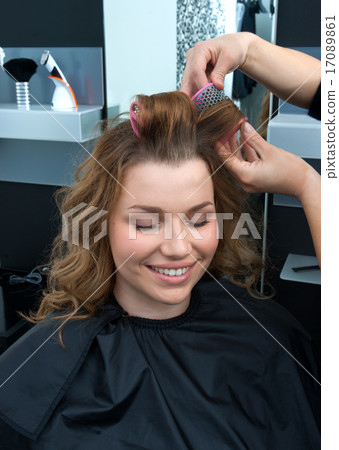 hair stylist curling woman hair in salon 17089861
