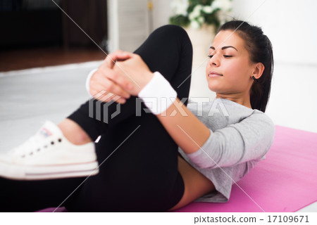 Fit woman doing aerobics gymnastics stretching exercises her leg lying on back warm up at home yoga 17109671