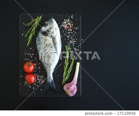 Fresh uncooked dorado or sea bream fish with vegetables, herbs and spices on black slate tray over Fresh uncooked dorado or sea bream fish with vegetables, herbs and spices on black slate tray over 17110056