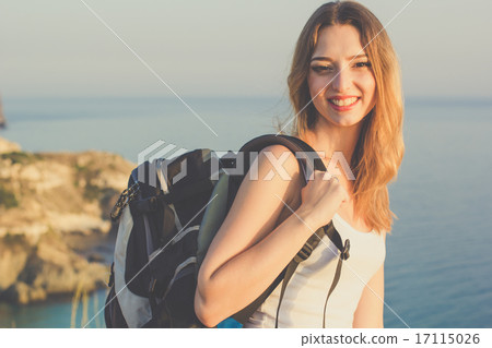 Smiling backpacker teen girl is standing on rock over sea Smiling backpacker teen girl is standing on rock over sea 17115026