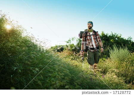 Young caucasian man with backpack walking on a green meadow 17128772