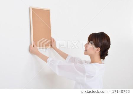 A woman trying to install a corkboard A woman trying to install a corkboard 17140763