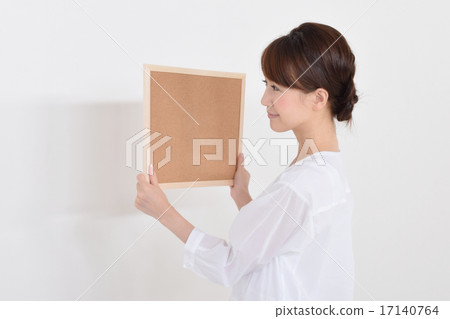 A woman trying to install a corkboard A woman trying to install a corkboard 17140764