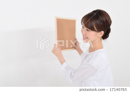 A woman trying to install a corkboard A woman trying to install a corkboard 17140765