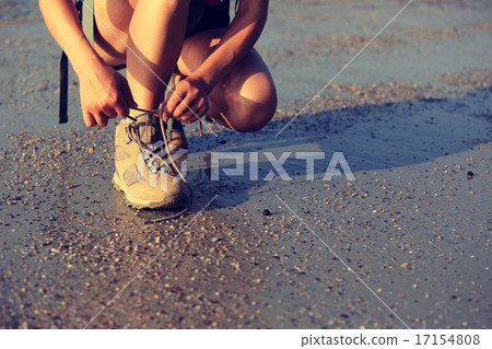 woman hiker tying shoelace on sunrise beach woman hiker tying shoelace on sunrise beach 17154808