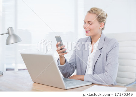 Businesswoman sending a text at her desk Businesswoman sending a text at her desk 17170349