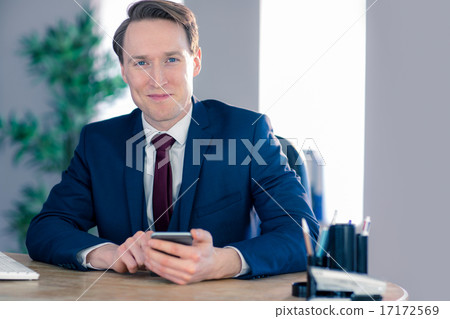 Confident businessman with smartphone looking at camera Confident businessman with smartphone looking at camera 17172569