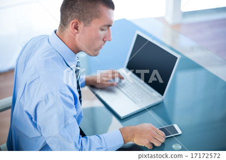Businessman using his laptop and his smartphone Businessman using his laptop and his smartphone 17172572
