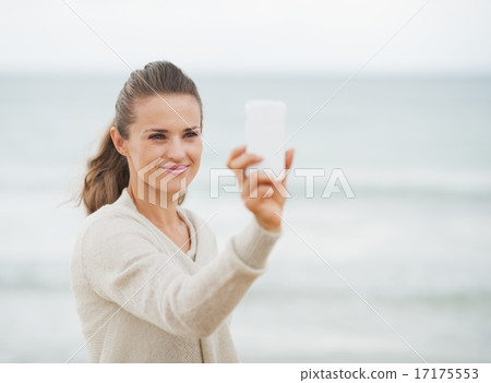 Happy young woman in sweater on beach taking photo using cell ph Happy young woman in sweater on beach taking photo using cell ph 17175553