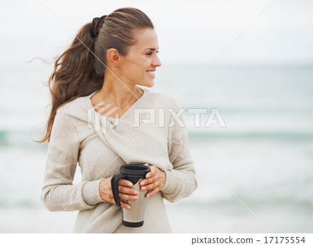 Happy young woman in sweater on beach with cup of hot beverage l Happy young woman in sweater on beach with cup of hot beverage l 17175554