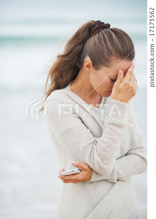 Stock Photo: Stressed young woman in sweater on beach with mobile phone