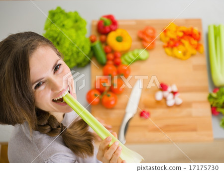 Happy young woman eating celery in modern kitchen Happy young woman eating celery in modern kitchen 17175730