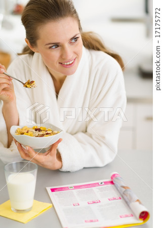 Thoughtful young woman in bathrobe eating breakfast in kitchen 17175772