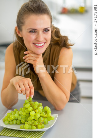 Happy young woman eating grape in kitchen 17175991
