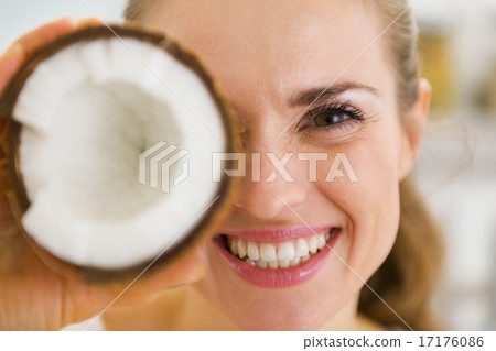 Happy young woman holding coconut piece in front of eye 17176086