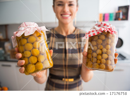 Closeup on young housewife showing jars with homemade gooseberry 17176758