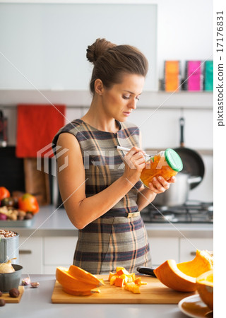 Young housewife signing jar of pickled pumpkin in kitchen Young housewife signing jar of pickled pumpkin in kitchen 17176831