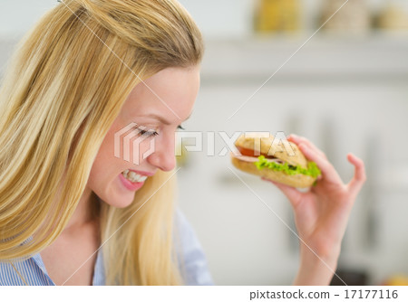 Happy young woman eating sandwich in kitchen Happy young woman eating sandwich in kitchen 17177116