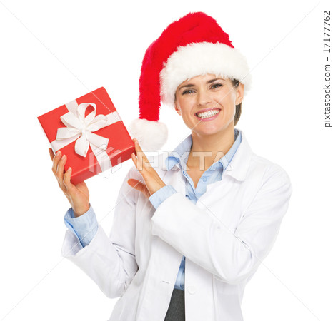 Happy doctor woman in santa hat showing christmas present box Happy doctor woman in santa hat showing christmas present box 17177762