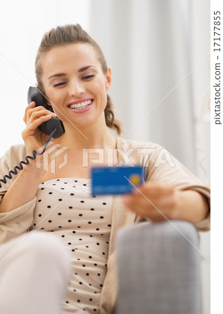 Happy young woman with credit card talking phone while sitting o 17177855