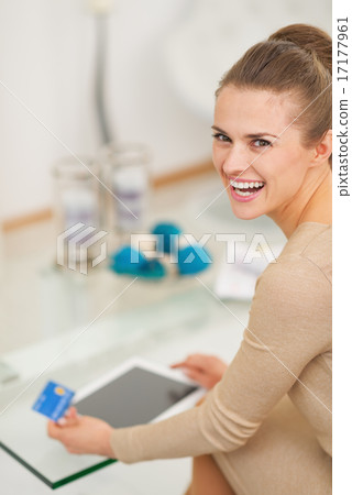 Smiling young housewife with credit card using tablet pc in livi Smiling young housewife with credit card using tablet pc in livi 17177961