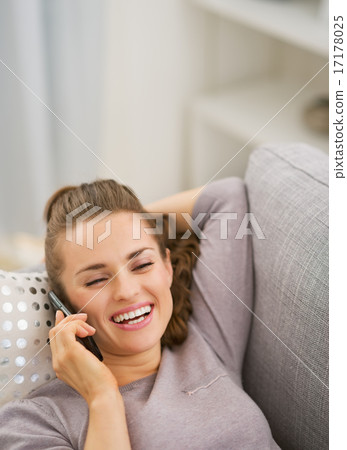 Happy young woman talking cell phone while laying on sofa Happy young woman talking cell phone while laying on sofa 17178025