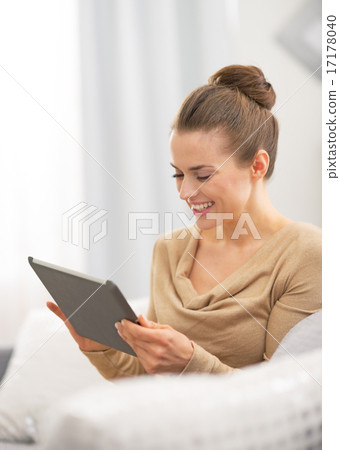 Smiling young woman using tablet pc while sitting on couch Smiling young woman using tablet pc while sitting on couch 17178040