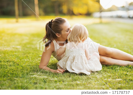 Mother kissing baby while sitting on meadow in park Mother kissing baby while sitting on meadow in park 17178737