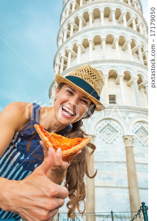Young woman with pizza showing thumbs up in front of leaning tow 17179050
